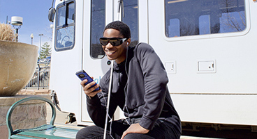 A man listens sitting in at a train stop listens to NFB-NEWSLINE on his phone.